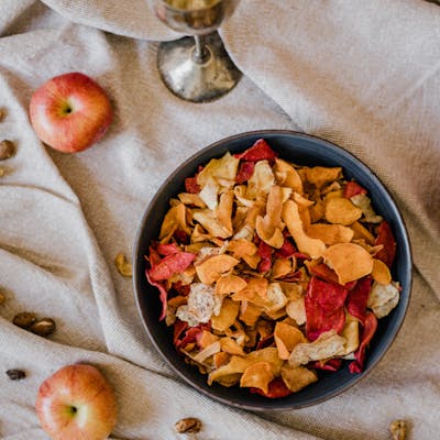 A beautiful composition featuring dried fruit snacks in a bowl with apples and a vintage goblet on fabric.