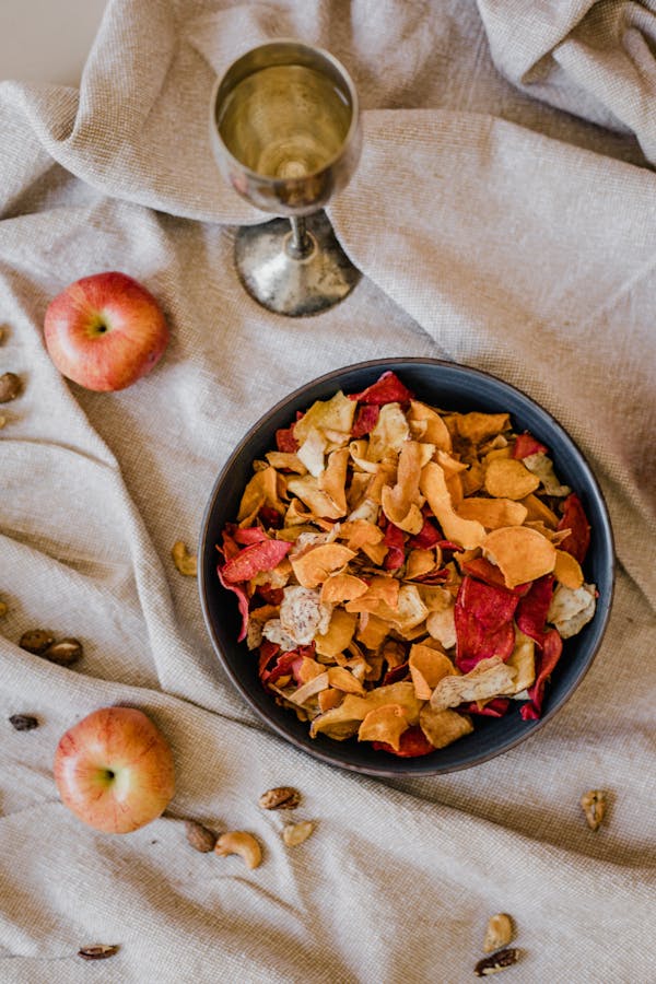 A beautiful composition featuring dried fruit snacks in a bowl with apples and a vintage goblet on fabric.