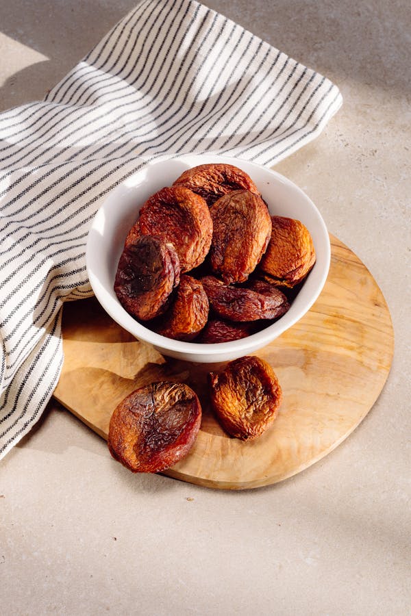 A bowl of dried apricots on a wooden board in warm sunlight, perfect for food blogging.