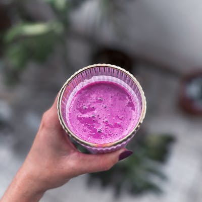A close-up of a hand holding a vibrant pink smoothie in a glass, perfect for a healthy lifestyle.