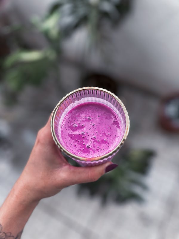 A close-up of a hand holding a vibrant pink smoothie in a glass, perfect for a healthy lifestyle.