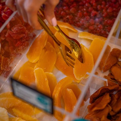 A hand selecting dried fruits with tongs in a market setting.