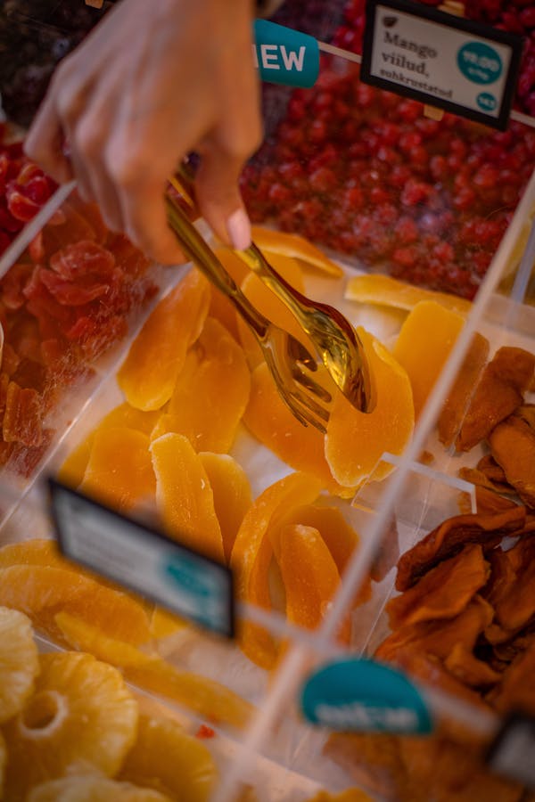 A hand selecting dried fruits with tongs in a market setting.