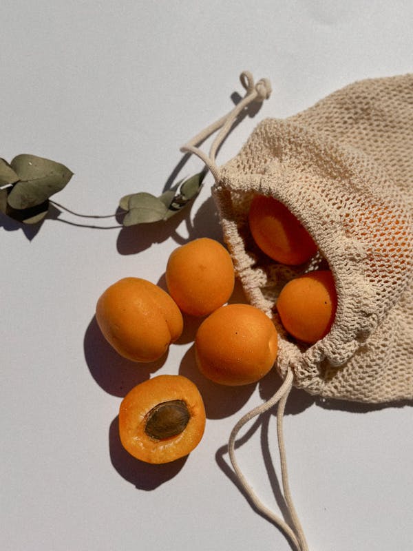 Close-up of apricots spilling from a string bag on a sunlit surface.
