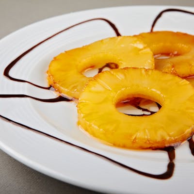 Delicious caramelized pineapple rings served on a white plate with chocolate drizzle.