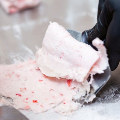 Detailed view of strawberry rolled ice cream being crafted on a frozen surface.