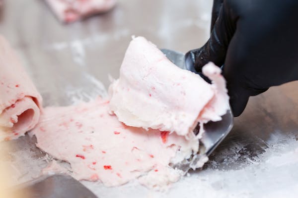 Detailed view of strawberry rolled ice cream being crafted on a frozen surface.