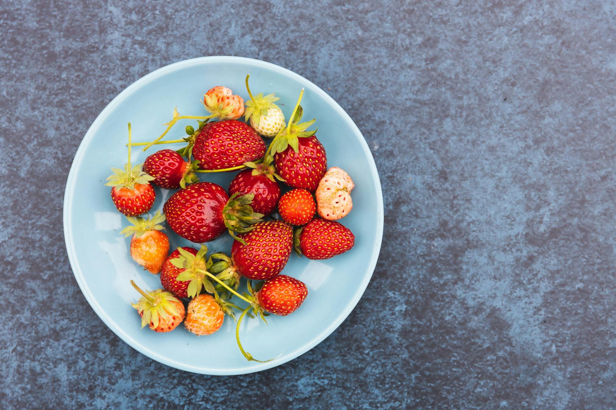 Fresh organic strawberries in a blue bowl on a textured surface, perfect for healthy living concepts.