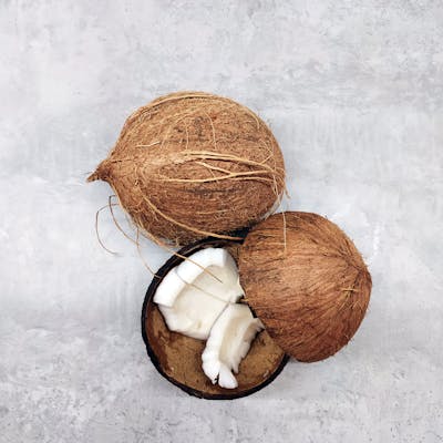 Fresh whole and sliced coconuts on a textured gray background, captured from above.