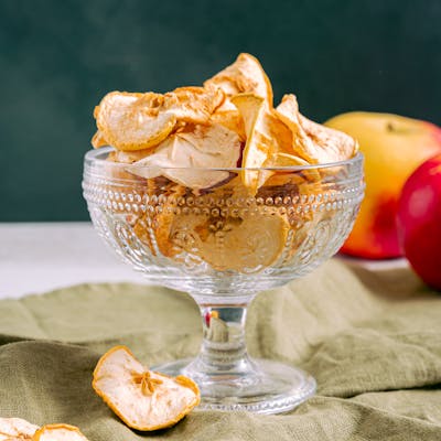 Stylish arrangement of dried apple slices in a decorative coupe glass on a soft green cloth.