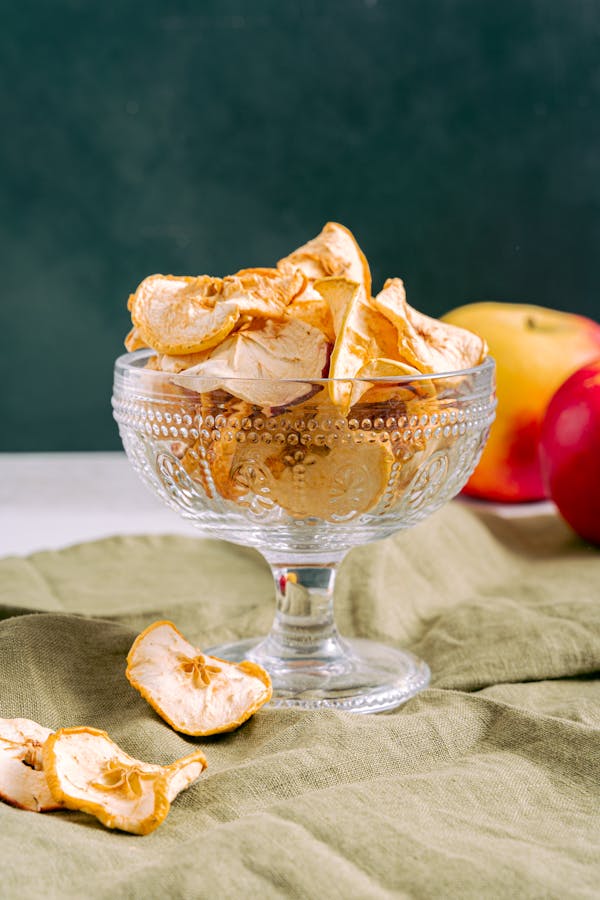 Stylish arrangement of dried apple slices in a decorative coupe glass on a soft green cloth.
