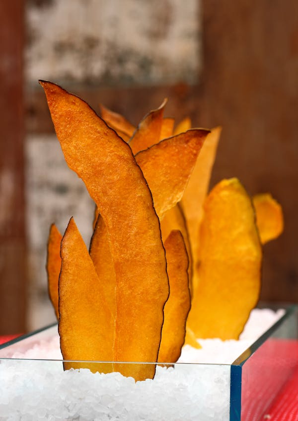 Vertical shot of crispy mango chips elegantly arranged in a clear container with a background blur.