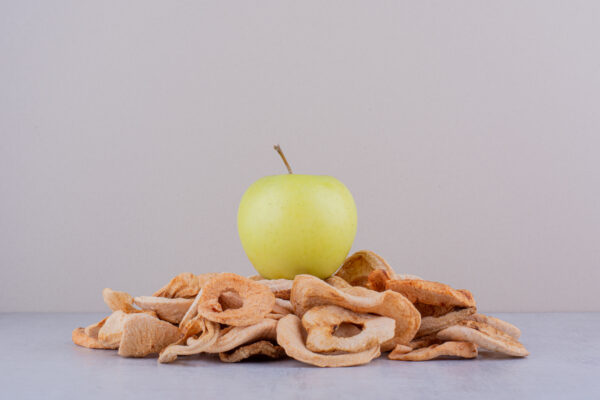 Green apple sitting on a pile of dried apple slices on white background